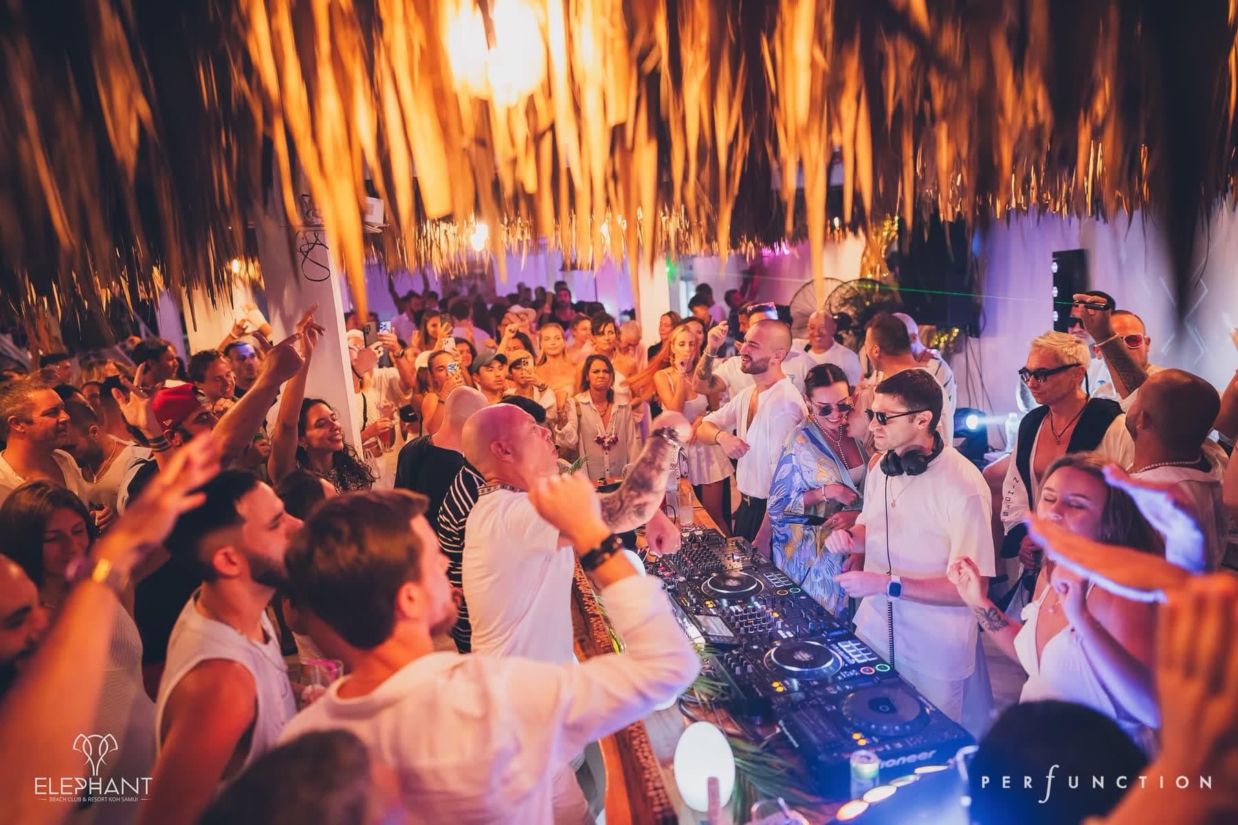 Crowd dressed in white with arms raised around the DJ booth at Elephant Beach Club, Chaweng Beach