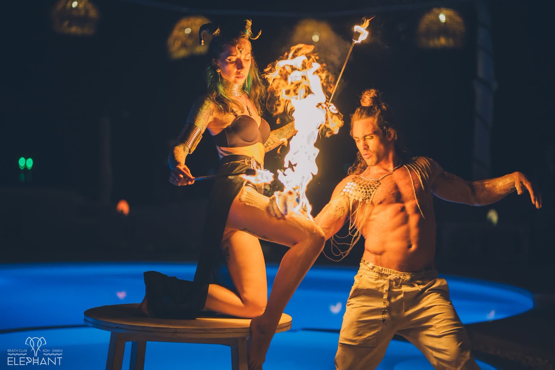 Two fire performers holding a lit prop beside the floodlit pool at Elephant Beach Club, Koh Samui