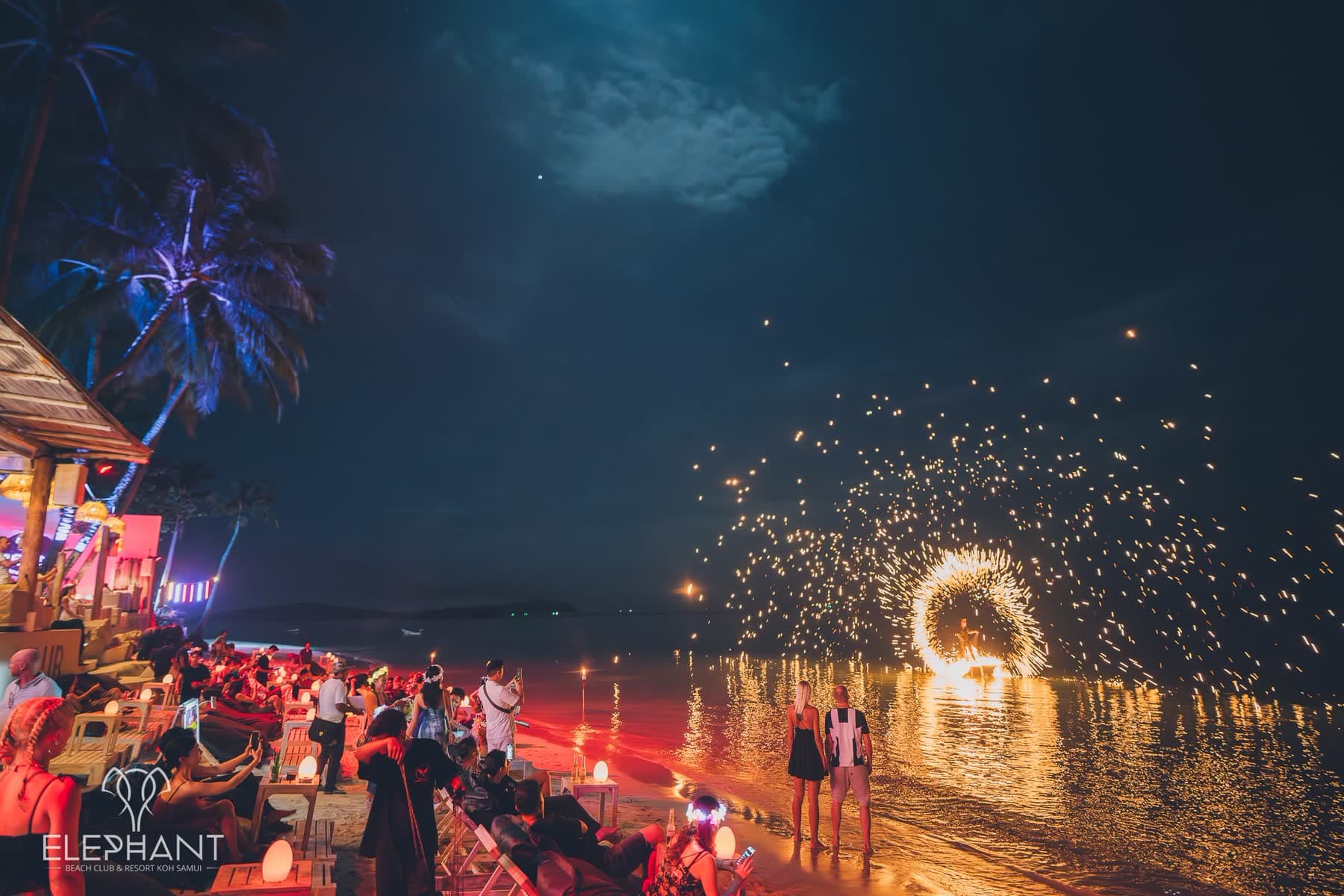 Chaweng Beach at night, a fire performer spinning a circle of flame reflected on the wet sand at Elephant Beach Club