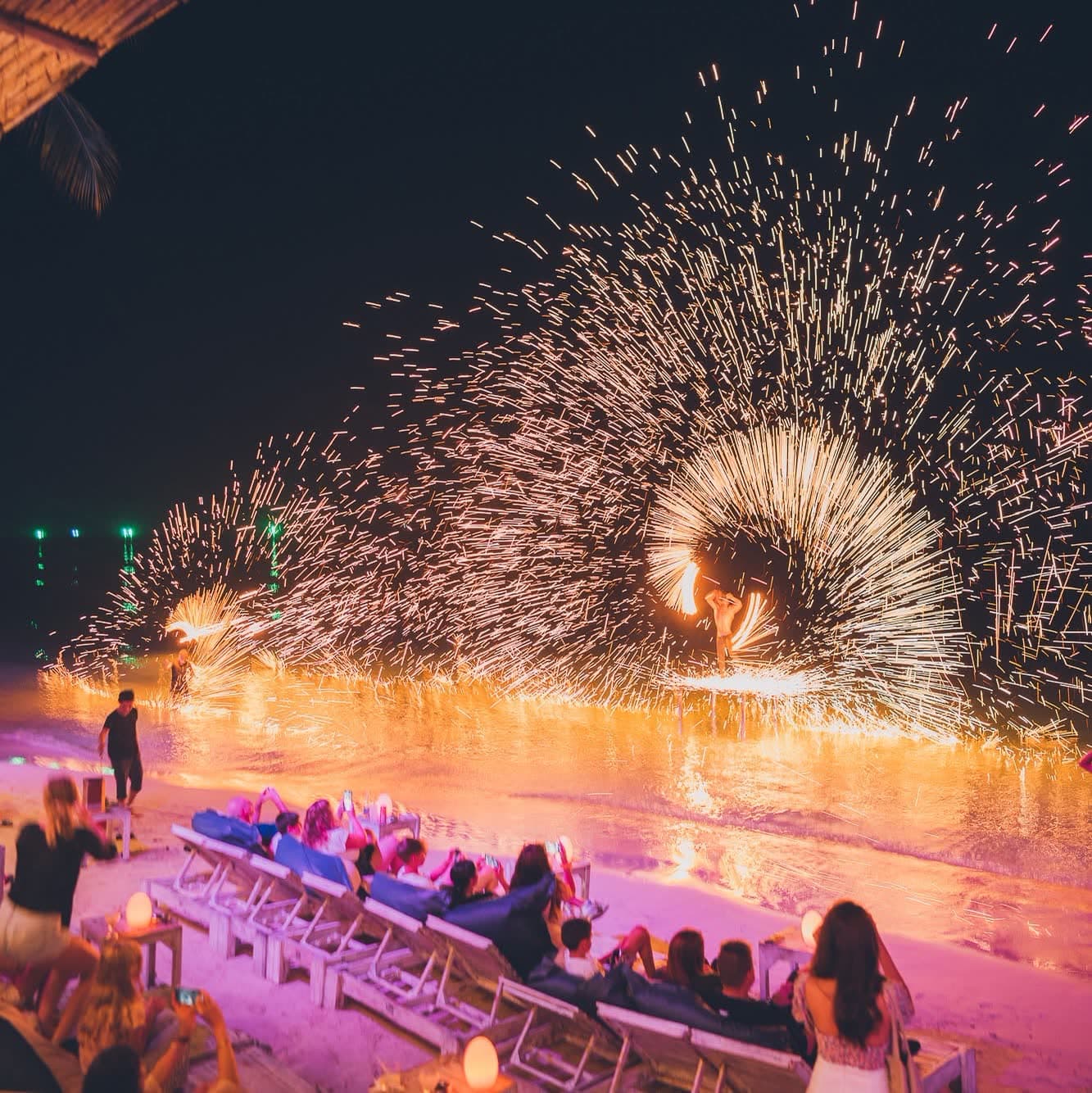 Fire show throwing a burst of sparks across the sand while guests watch from the sunbeds at Elephant Beach Club, Chaweng Beach