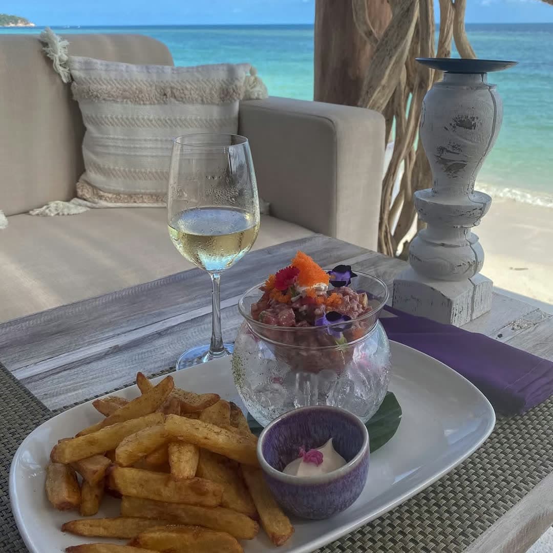 Tuna tartare served in a glass bowl over crushed ice with fries and a glass of white wine, the sea in the background, at Elephant