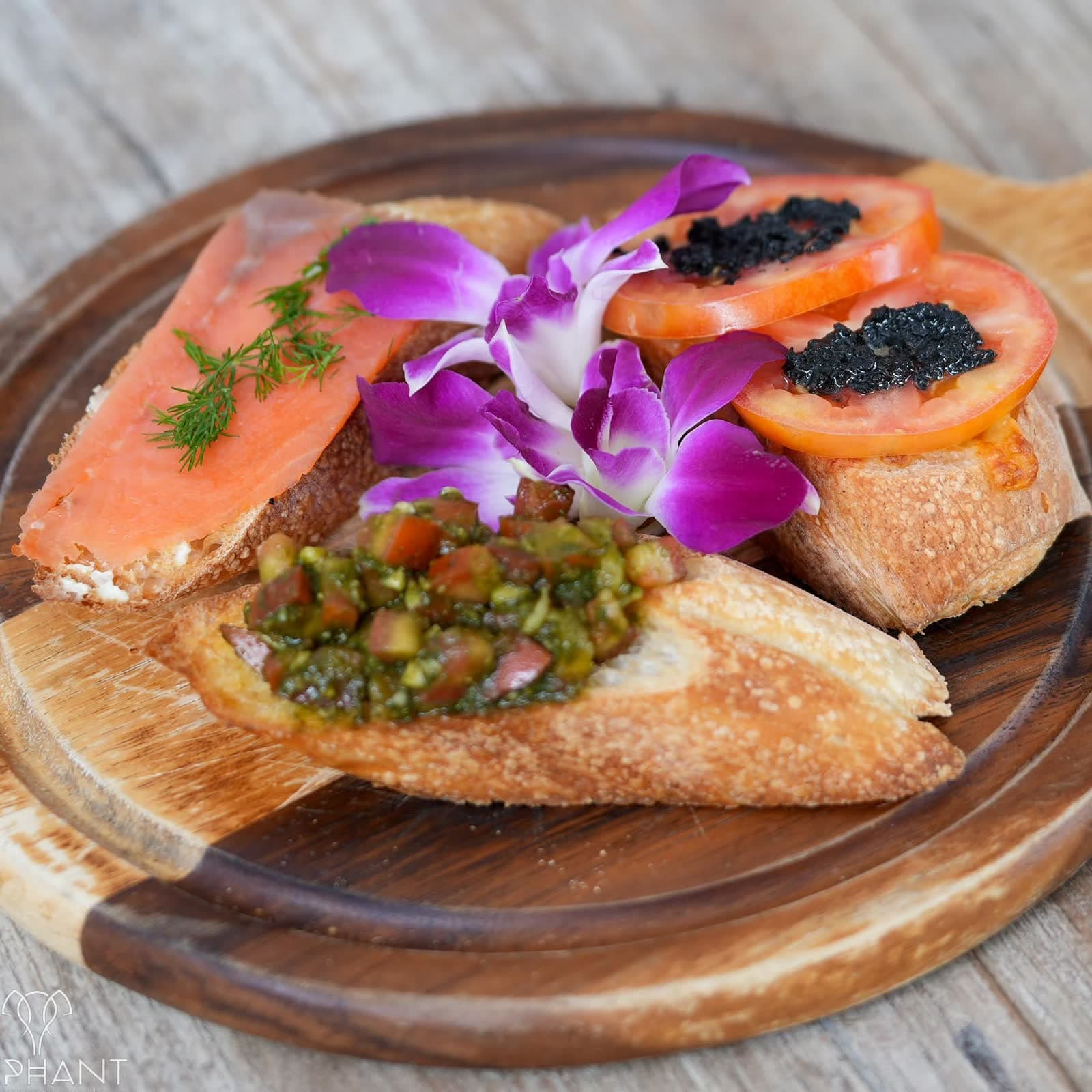 Smoked salmon and caviar bruschetta with an orchid on a wooden board at Elephant, Chaweng Beach
